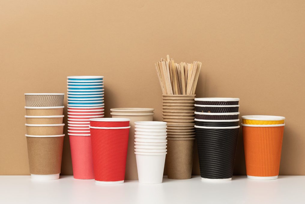 stacks of assorted disposable paper cups for drinks, coffee and tea on a white table. Takeaway beverage container